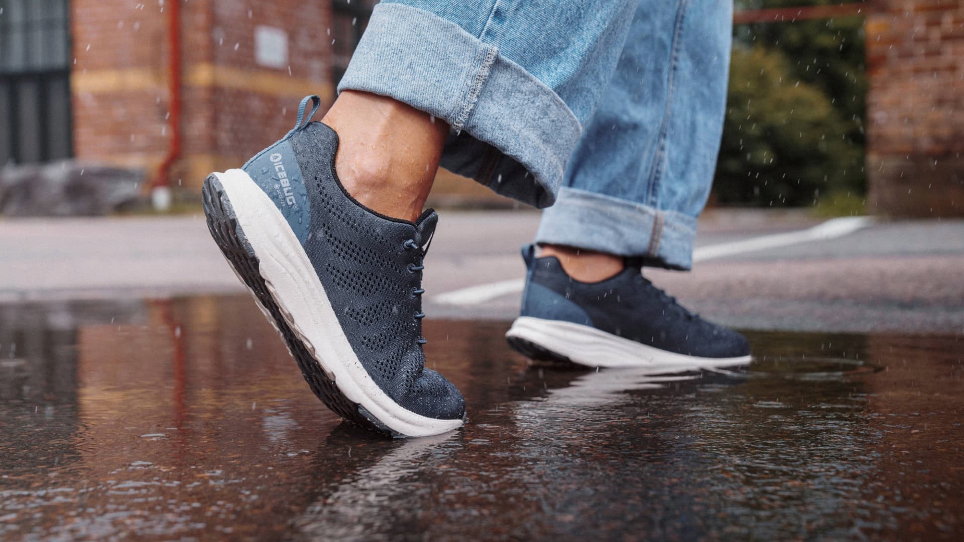 Person wearing rolled-up jeans and blue sneakers stepping in a puddle on a rainy day.